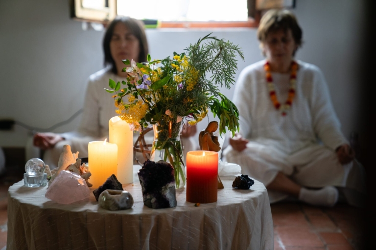 Altare con pietre e piante, sullo sfondo due persone vestite di bianco in meditazione, rappresenta uno spazio sacro per cerimonie sciamaniche