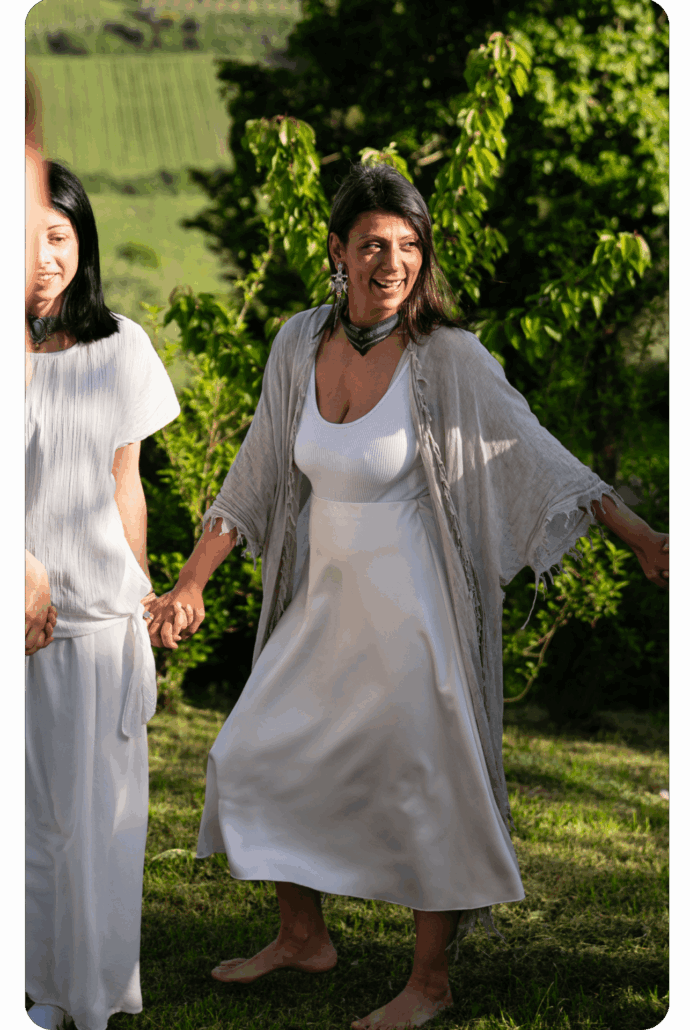 Sonia La Marca partecipa sorridente a un cerchio rituale all’aperto, camminando a piedi nudi in un prato, simbolo del suo approccio autentico e connesso alla Madre Terra.